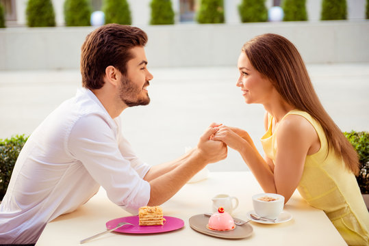 Side profile photo of pretty lovers on a honey moon, having brunch outdoors on nice terrace, well dressed, smiling, hiolding hands