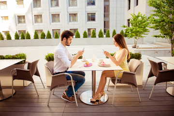 Internet addicted young couple is having brunch in nice cafe with modern interior, light summer terrace with green nice plants