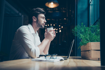 Time for inspiration and rest. Low angle photo of young freelancer, relaxing, having coffee, he is dreaming and enjoying, sitting in a modern cafe