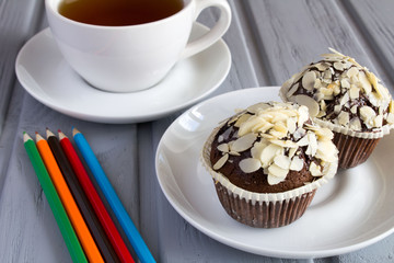 Chocolate muffins, tea and pencils on the grey wooden background