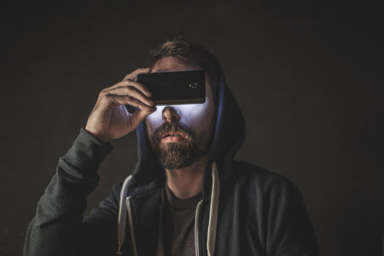 Technology man. Odd portrait of young man illuminated with mobile phone.