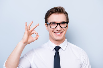 Success concept. Young handsome geek in a formal wear, black glasses, stands on pure light background, gesturing ok sign