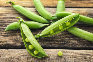 Pods of green peas and pea on a dark wooden surface,