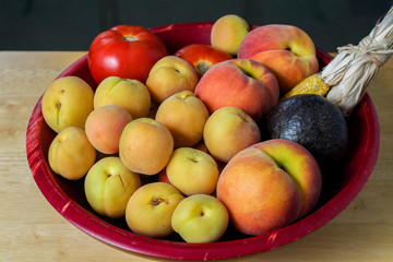 A bowl of fruits harvested in California in the summer, in red basket,  decorated with indian corn
