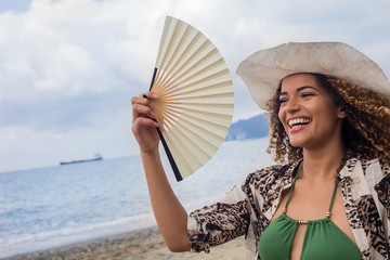 Happy young woman smiling and holding fan on the beach