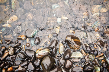 Black sea stones background. Glossy round river rocks and wave surfing, Thailand. wanderlust and unplugged. Top view. Close up.