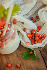 Homemade strawberry yogurt with fresh wild strawberries and mint in a jar on a wooden board, selective focus