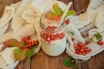 Fresh milk yoghurt with wild strawberries and granola served in a glass jar with mint leaves on white wooden table with striped red napkin. Healthy summer breakfast concept. Top view.