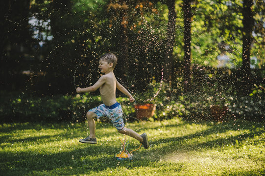 Little boy running through crazy sprinklers in the backyard