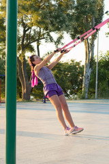 workout with suspension straps In the outdoor gym, fit woman training early in morning on the park, sunrise background  