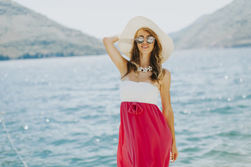 Young attractive woman with a hat and glasses poses by the sea