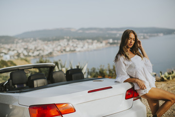 Young attractive woman poses next to a  cabriolet at seaside