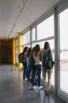 Group of teenager students looking outside the window of the corridor