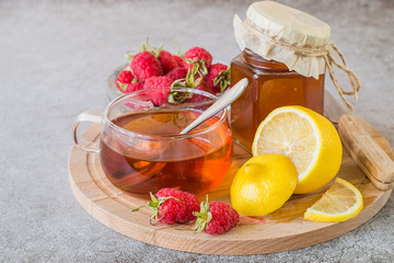  Prevention and treatment of influenza and colds. Ripe raspberries, fresh lemon, a glass jar with honey and a mug with hot tea on a round wooden board on a light background.
Used in folk medicine.