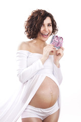 pregnant woman in a white dress holding a tiny baby shoes