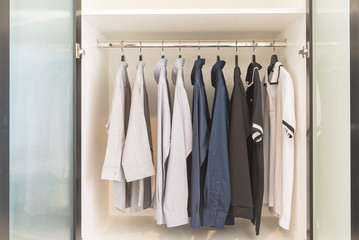 clothes hanging on rail in wooden white wardrobe