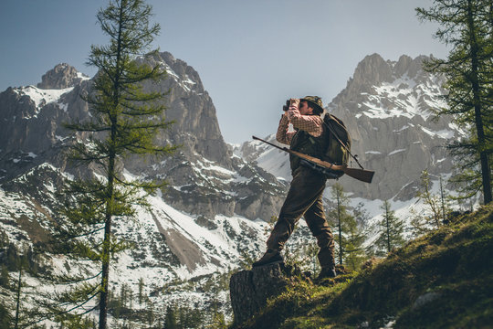 hunter standing on a trunk with his shotgun looking through binocular