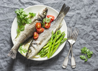 Baked sea bass with asparagus and tomatoes. Healthy diet food concept. On a gray background, top view