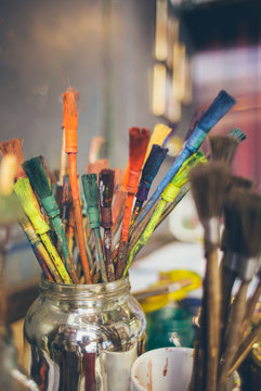 Used paintbrushes and utensils in a glass on a table