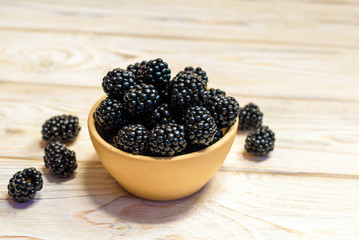 Close up of ripe blackberries in a white ceramic bowl over rustic wooden background