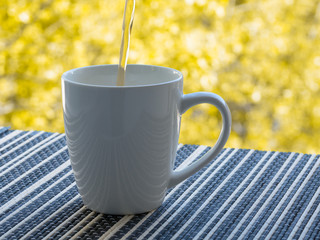 Drink poured into mug on the table by the open window.