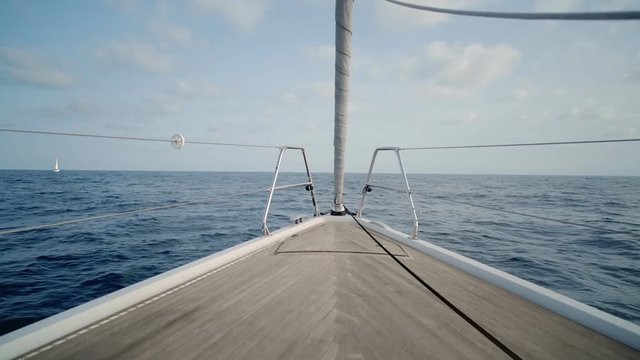 Peaceful view on nose of clean white sailing boat with parquet floor and folded genoa or overlapping jib, using only motors going forward in sea or ocean at evening or early morning