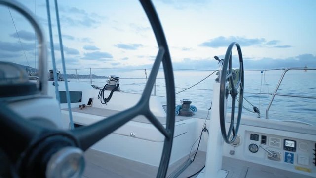 Close up on carbon steering wheels of sailing boat gently spinning controlled by autopilot programmed for home port course. Soft twilight evening light at summer in sea.