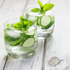 Summer refreshing detox cocktail. Water with cucumber,mint  and ice in glass on a white wooden background. Rustic style.