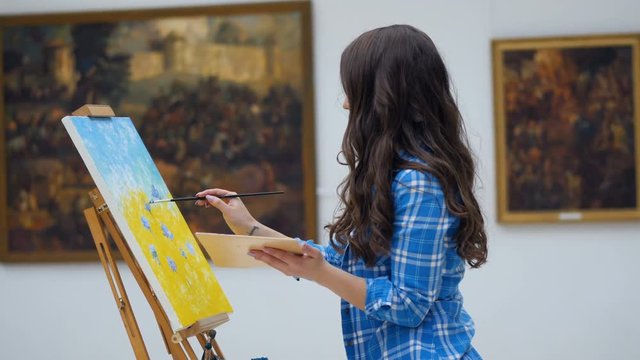 Female artist painting a picture on canvas. Art gallery background. 4K.