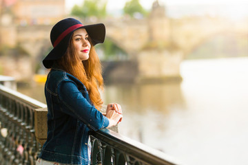 Portrait of the beautiful fashionable girl with hat on embankment in summer day