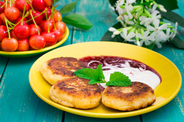 Cheese pancake with jam and fresh cherries. Wooden turquoise background. Top view. Close-up