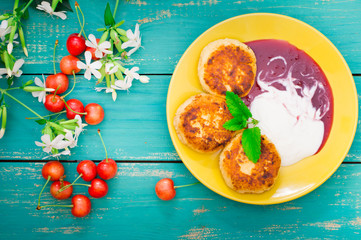 Cheese pancake with jam and fresh cherries. Wooden turquoise background. Top view. Close-up
