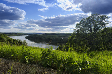 Rural summer landscape with river, forest, green fields, blue sky and dramatic clouds, countryside, high angle view, natural background