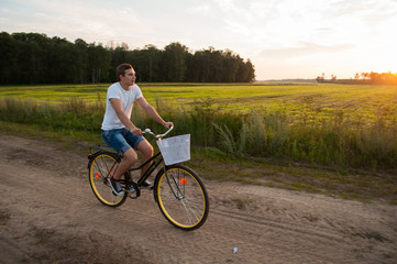 Obraz premium The guy rides a Bicycle along a country road at sunset,