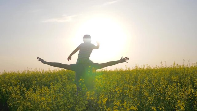 family going in meadow flowers in sunlight, men with boy on neck moving across blossom, daddy and children go by field with raised arms, father carries son on shoulders walking through field,