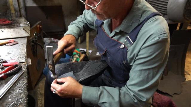 Shoemaker repairing a shoe in workshop 4k. nail the heel cap to the heel