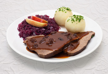 Sauerbraten mit Rotkohl und Knödeln - Tellergericht auf weißer Tischdecke