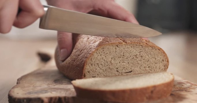 Slow motion slide shot of young female hands slicing rye wheat rustic bread on cutting board
