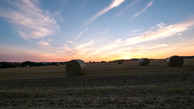 Time lapse footage of hay bail harvesting in golden field landscape during sunset.