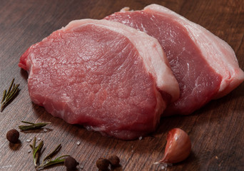 raw pork chop steak and garlic, pepper on the brown wooden table background. rustic kitchen table
