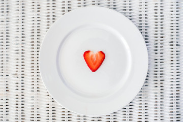 A slice of heart shaped strawberry on a pure white plate