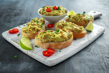 Homemade Guacamole toast with chili pepper, parsley on white wooden board