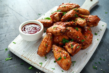 Baked chicken wings with sesame seeds and sweet chili sauce on white wooden board.