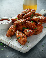 Baked chicken wings with sesame seeds, beer and sweet chili sauce on white wooden board.