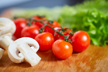 Fresh and tasty tomatoes, salad, onion, champignon on wooden cutting board
