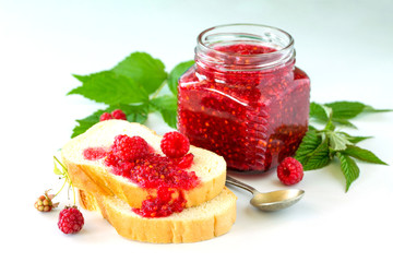 Homemade jam and white bread. Glass jar with raspberry jam on a white background. Preserved berry.