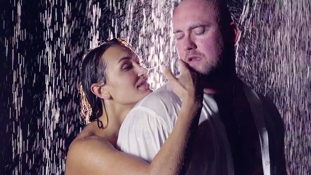 large bald man in a white shirt stands with his woman in the shower under the streams of water. his clothes were wet on the head flow streams of water.