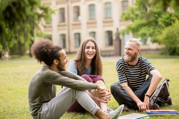 Happy laughing students at University garden. Three studens having lively conversation sitting on...