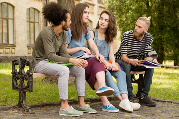 Students sitting on bench telling stories. Young boys and girls having rest after lectures.