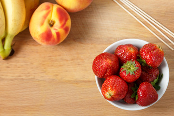 Preparation for a fruit cocktail on a cutting board of bananas, kiwi, strawberries, peaches, coconuts. View from above.